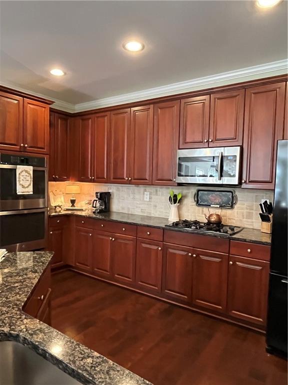 kitchen featuring dark wood-type flooring, dark stone countertops, backsplash, recessed lighting, and appliances with stainless steel finishes