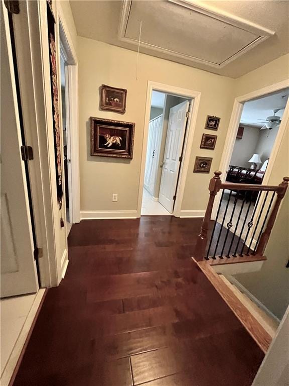 hall featuring an upstairs landing, attic access, dark wood-type flooring, and baseboards