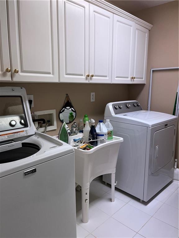 washroom with washer and dryer, light tile patterned floors, cabinet space, and a sink