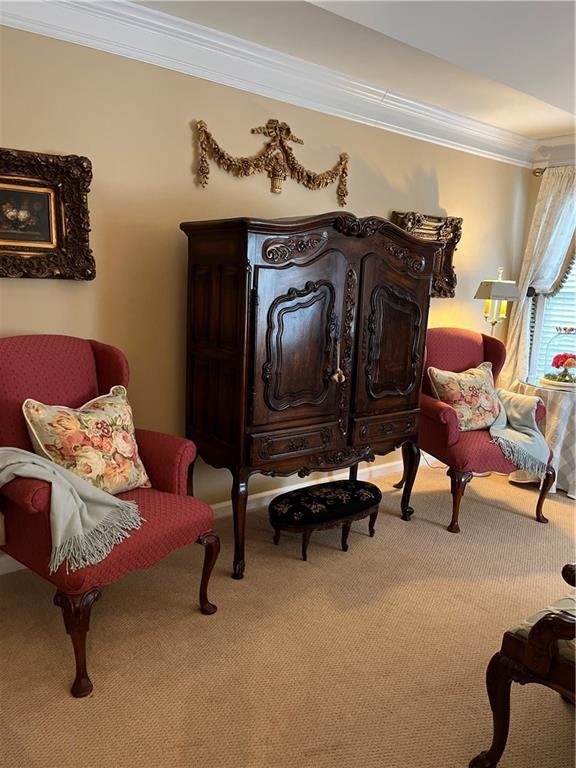 living area with crown molding and carpet