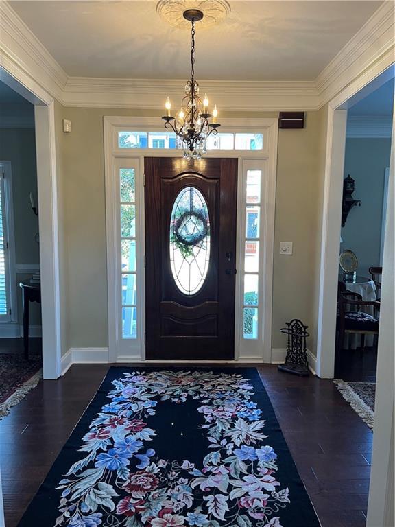 foyer entrance featuring crown molding, baseboards, dark wood-style flooring, and a chandelier