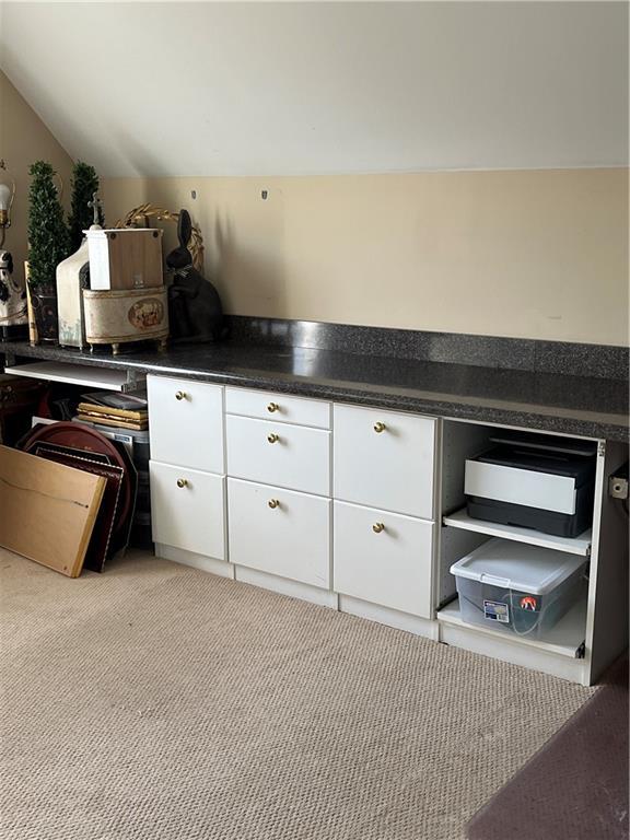 kitchen with light colored carpet, dark countertops, vaulted ceiling, and white cabinetry