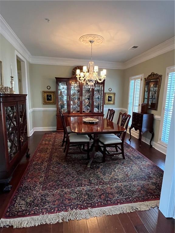 dining area with a notable chandelier, wood finished floors, visible vents, and ornamental molding