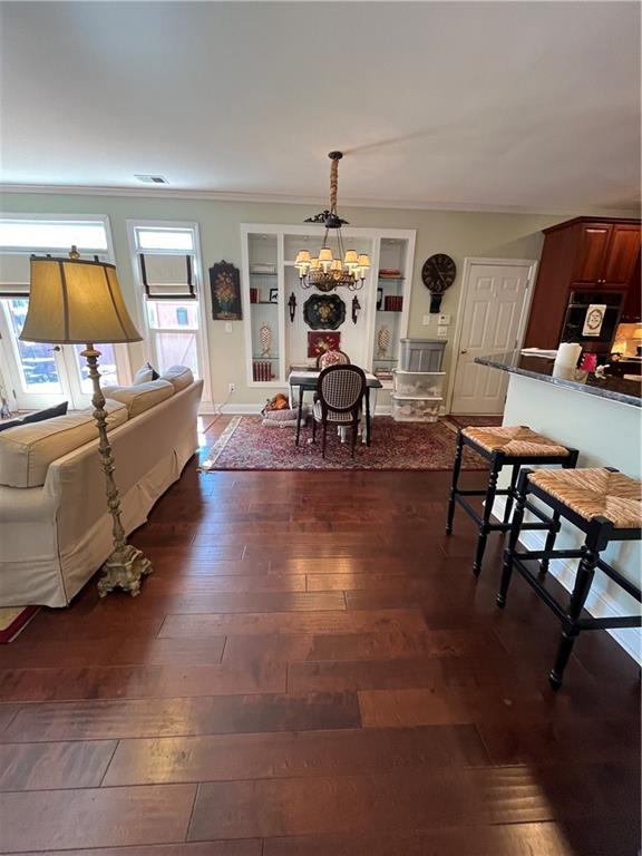 living area with baseboards, dark wood-type flooring, a chandelier, and ornamental molding