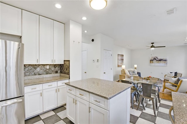 kitchen with stainless steel fridge, ceiling fan, light stone countertops, white cabinets, and decorative backsplash