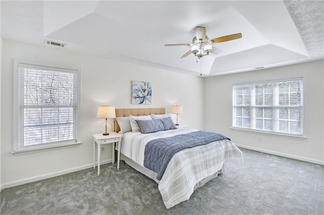 carpeted bedroom featuring a raised ceiling, ceiling fan, and multiple windows