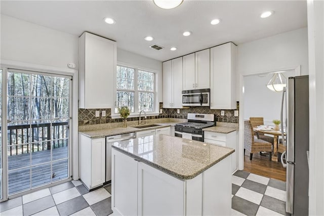 kitchen with sink, appliances with stainless steel finishes, a center island, light stone countertops, and white cabinets