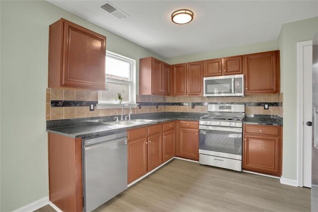 kitchen with light hardwood / wood-style floors, stainless steel appliances, sink, and tasteful backsplash