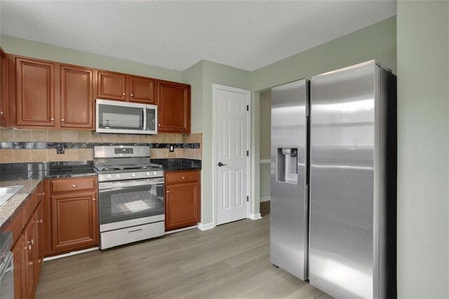 kitchen with appliances with stainless steel finishes, light hardwood / wood-style floors, and decorative backsplash