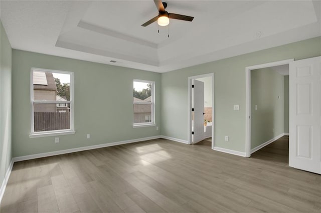 unfurnished bedroom featuring multiple windows, connected bathroom, light wood-type flooring, and ceiling fan