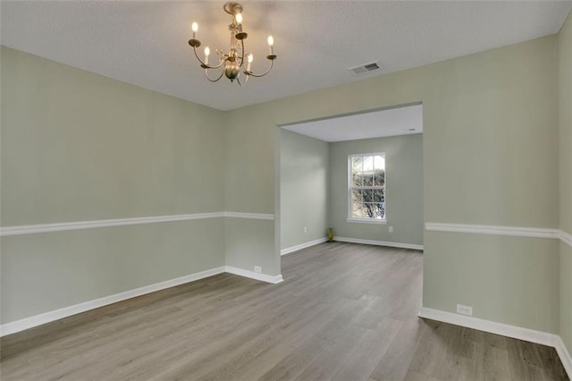 empty room featuring an inviting chandelier, a textured ceiling, and hardwood / wood-style flooring