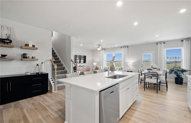 kitchen with white cabinets, dishwasher, an island with sink, sink, and light hardwood / wood-style flooring