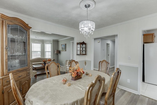 dining area featuring crown molding, a notable chandelier, a textured ceiling, and light wood-type flooring