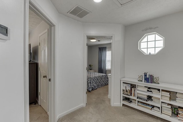 hallway with light colored carpet and a textured ceiling