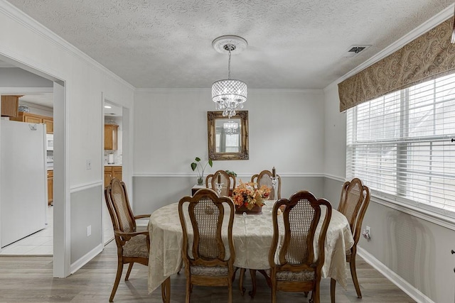 dining space featuring crown molding, a textured ceiling, a notable chandelier, and light wood-type flooring