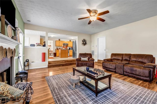 living area with a textured ceiling, ceiling fan, a fireplace, and light wood finished floors