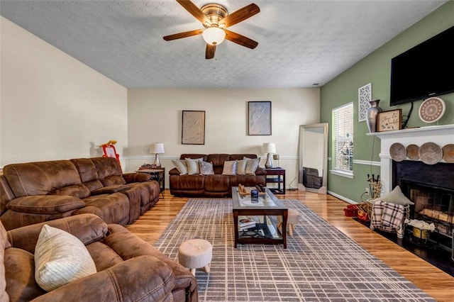 living room featuring a textured ceiling, a stone fireplace, wood finished floors, and ceiling fan