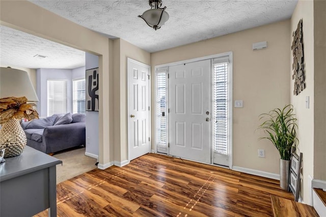 foyer entrance with baseboards, a textured ceiling, and wood finished floors