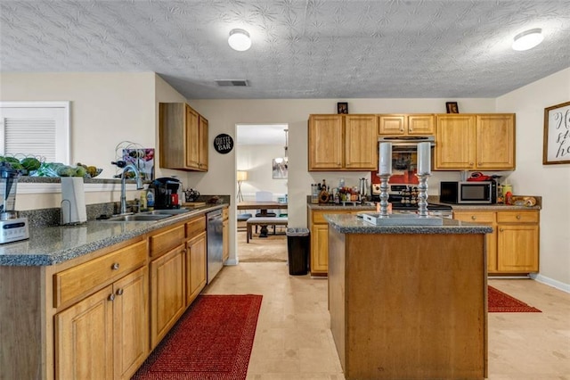 kitchen featuring visible vents, a sink, a center island, dark stone counters, and appliances with stainless steel finishes