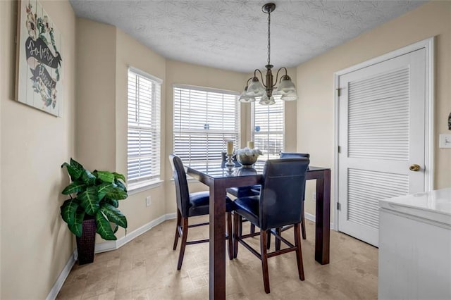 dining space featuring baseboards, a textured ceiling, a healthy amount of sunlight, and a chandelier