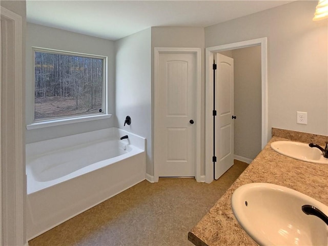 bathroom featuring a garden tub, double vanity, a sink, and baseboards