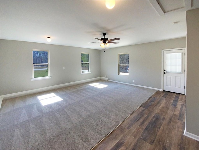 empty room with dark wood-style floors, dark carpet, ceiling fan, and baseboards