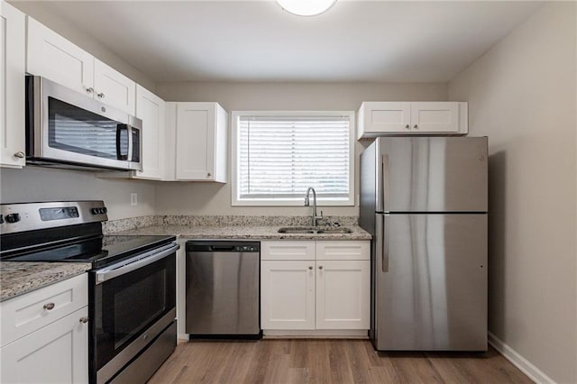 kitchen featuring white cabinets, appliances with stainless steel finishes, light stone counters, and sink