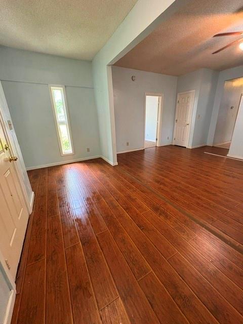 unfurnished room with a textured ceiling, wood-type flooring, ceiling fan, and baseboards