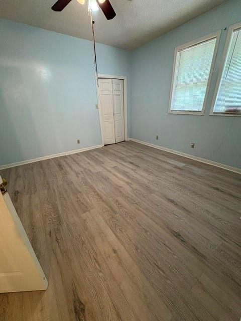 unfurnished bedroom with wood finished floors, baseboards, a closet, and ceiling fan