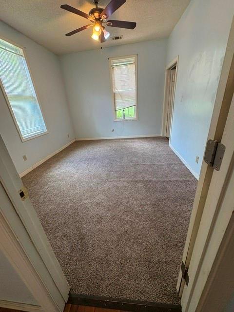 empty room featuring a textured ceiling, a ceiling fan, carpet floors, and baseboards