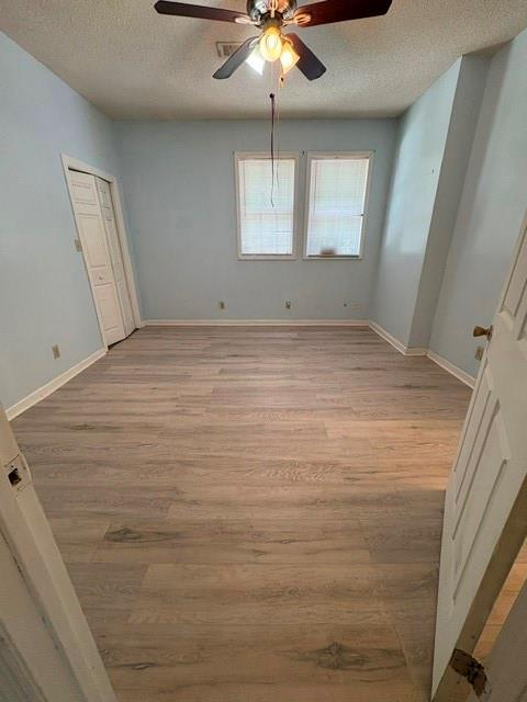 empty room with a textured ceiling, light wood-style flooring, a ceiling fan, and baseboards