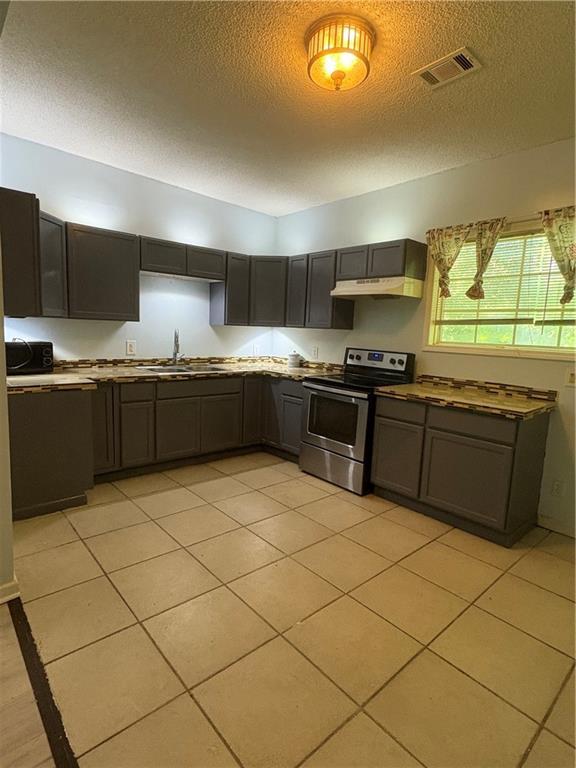 3831 Fairmont Ave, Macon, GA 31204 - kitchen with stainless steel range with electric stovetop, a sink, a textured ceiling, under cabinet range hood, and light tile patterned floors
