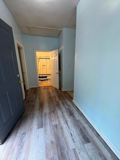corridor with attic access, wood finished floors, baseboards, and a textured ceiling