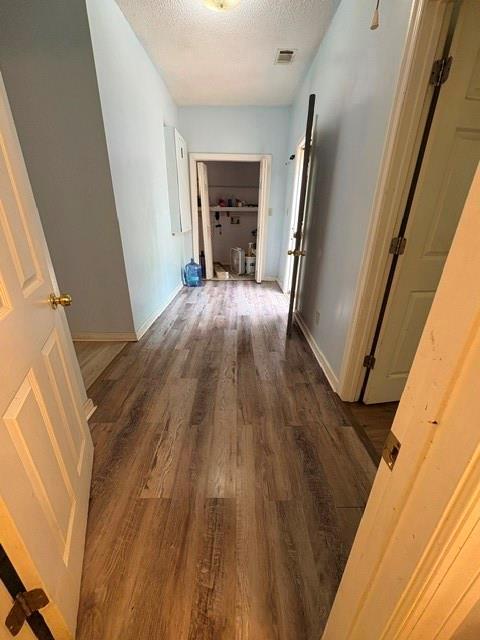 corridor with wood finished floors, a textured ceiling, and baseboards