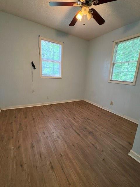 empty room with plenty of natural light, wood finished floors, baseboards, and a textured ceiling