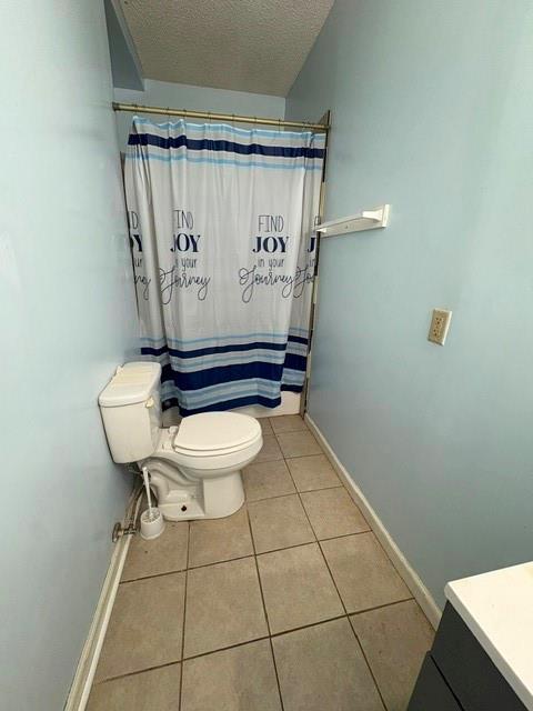 bathroom featuring tile patterned floors, toilet, a textured ceiling, baseboards, and a shower with curtain