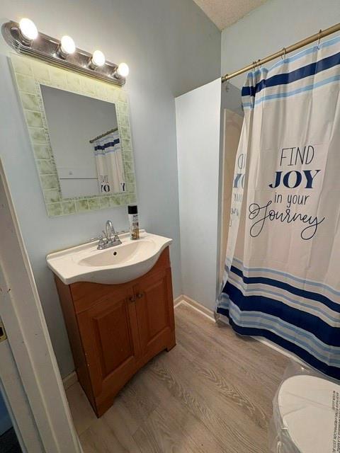 full bathroom with wood finished floors, vanity, curtained shower, and baseboards
