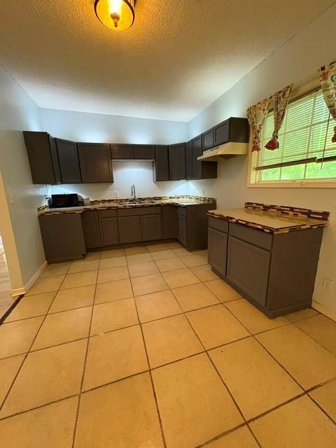 kitchen with a sink, a textured ceiling, baseboards, and light tile patterned flooring