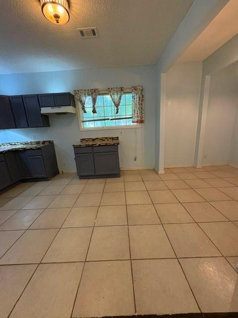 kitchen featuring a textured ceiling, light tile patterned flooring, and under cabinet range hood