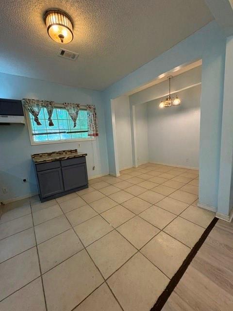 unfurnished dining area with a textured ceiling, light tile patterned flooring, and baseboards