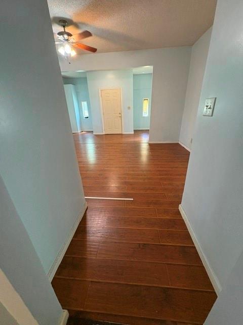 empty room featuring hardwood / wood-style flooring, ceiling fan, baseboards, and a textured ceiling
