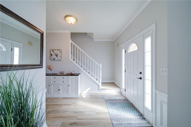 foyer entrance with light wood-style floors, crown molding, baseboards, and stairs