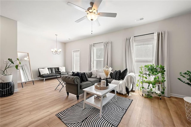 living room with ceiling fan with notable chandelier, baseboards, visible vents, and light wood-style floors