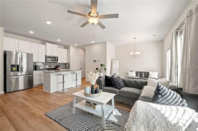 living room featuring recessed lighting, light wood finished floors, and ceiling fan with notable chandelier