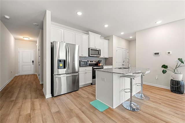 kitchen with light wood finished floors, a kitchen bar, stainless steel appliances, and a sink