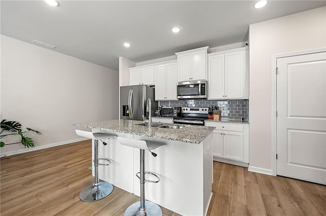 kitchen with stainless steel appliances, light wood-style floors, a sink, and decorative backsplash