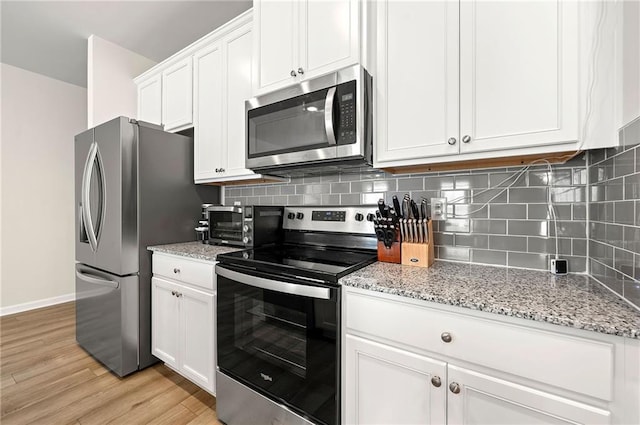 kitchen with light wood finished floors, tasteful backsplash, light stone countertops, stainless steel appliances, and white cabinetry