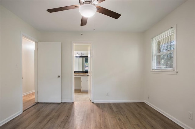 unfurnished bedroom with wood finished floors, ensuite bathroom, and baseboards
