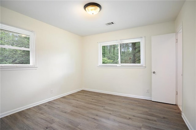 empty room featuring wood finished floors, visible vents, and baseboards