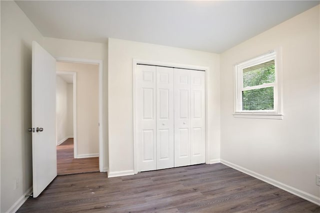 unfurnished bedroom with a closet, baseboards, and dark wood-type flooring